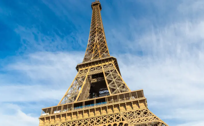 Vista cercana de la Torre Eiffel en París, mostrando su estructura metálica contra un cielo azul con nubes.