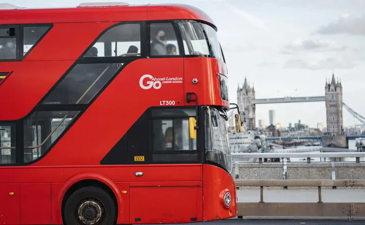 Autobús rojo de dos pisos cruzando Londres con el Puente de la Torre al fondo, típico del transporte londinense.