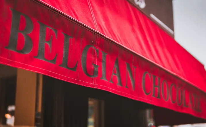 Toldo rojo de tienda con el texto "BELGIAN CHOCOLATE" en letras grandes y negras, anunciando chocolates belgas.