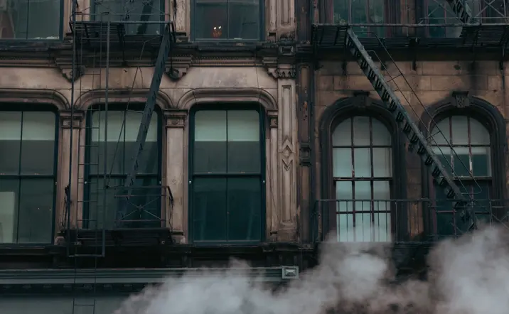 Edificios antiguos de ladrillo en Nueva York, con escaleras de incendio exteriores y vapor saliendo a la altura de la calle.