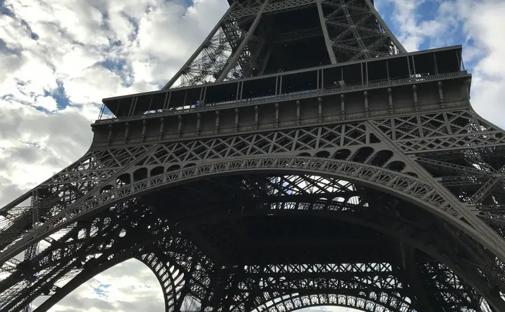 Vista desde la base de la Torre Eiffel en París, Francia, mostrando la estructura metálica contra un cielo parcialmente nublado.