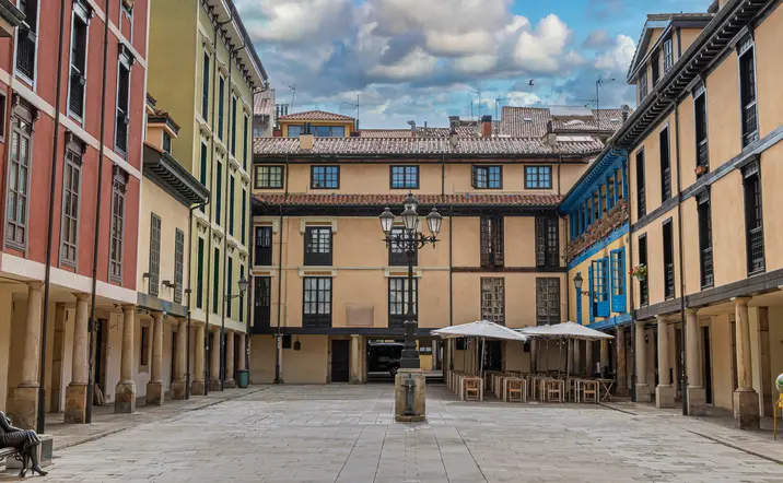 Plaza del Fontán en Oviedo, Asturias, con fachadas de colores, soportales tradicionales y una estatua en primer plano.