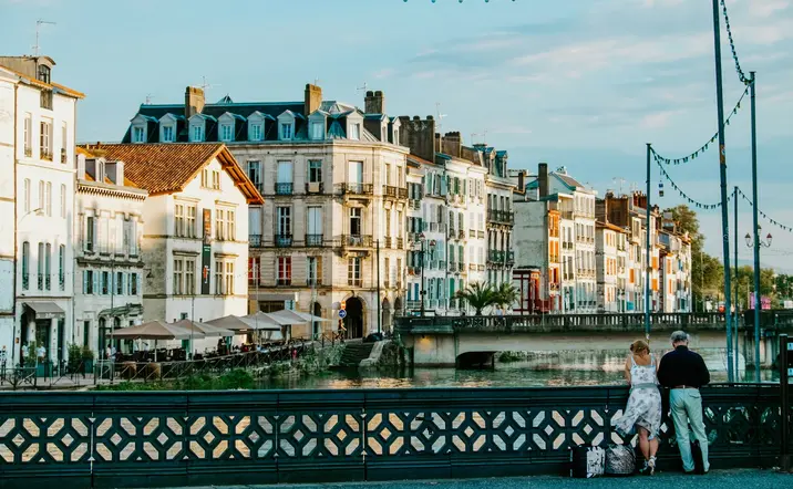 Río y casas al atardecer en Bayona, con parejas apoyadas en el puente.