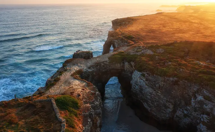Vista aérea de la Playa de las Catedrales al atardecer, con sus arcos de roca bañados por el mar Cantábrico.