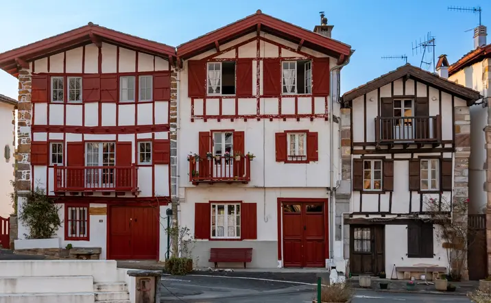 Fachadas típicas de casas vascas con madera roja y balcones floridos en el centro histórico de Espelette.
