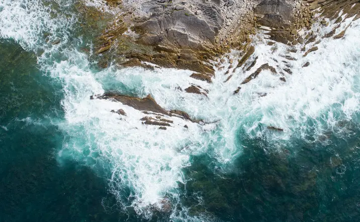 Vista aérea de las olas turquesas rompiendo contra las rocas y el acantilado en la costa de San Juan de Luz.