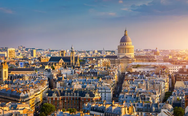 Ciudad de París al atardecer, mostrando un horizonte con edificios emblemáticos y un cielo teñido de tonos cálidos.